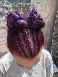 A woman with a glittery purple unicorn braid and space bun hairstyle.